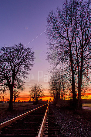 A Winter Sunset on a Railroad Track with the Moon and a Jet Trail