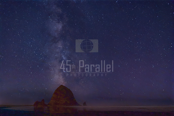 The Milky Way rises behind Haystack Rock like a column of smoke from a rumbling volcano.